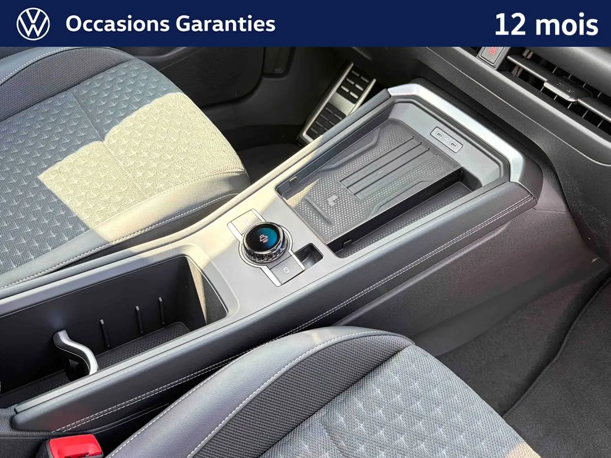 Vue intérieure rapprochée du console central et sièges avant gris du Volkswagen T-Roc noir, avec molette de sélection de vitesse.