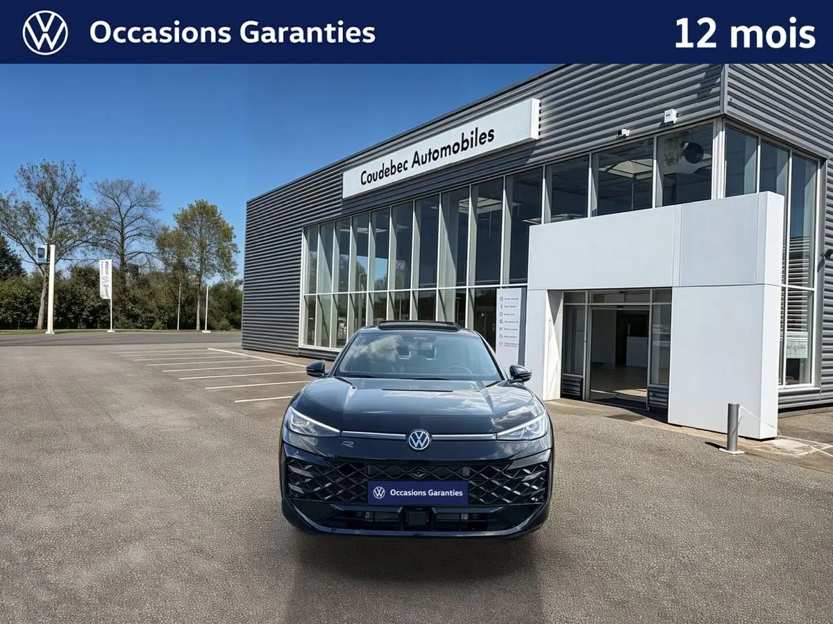 Vue de face du Volkswagen T-Roc noir métallisé avec toit ouvrant panoramique, devant un bâtiment moderne.