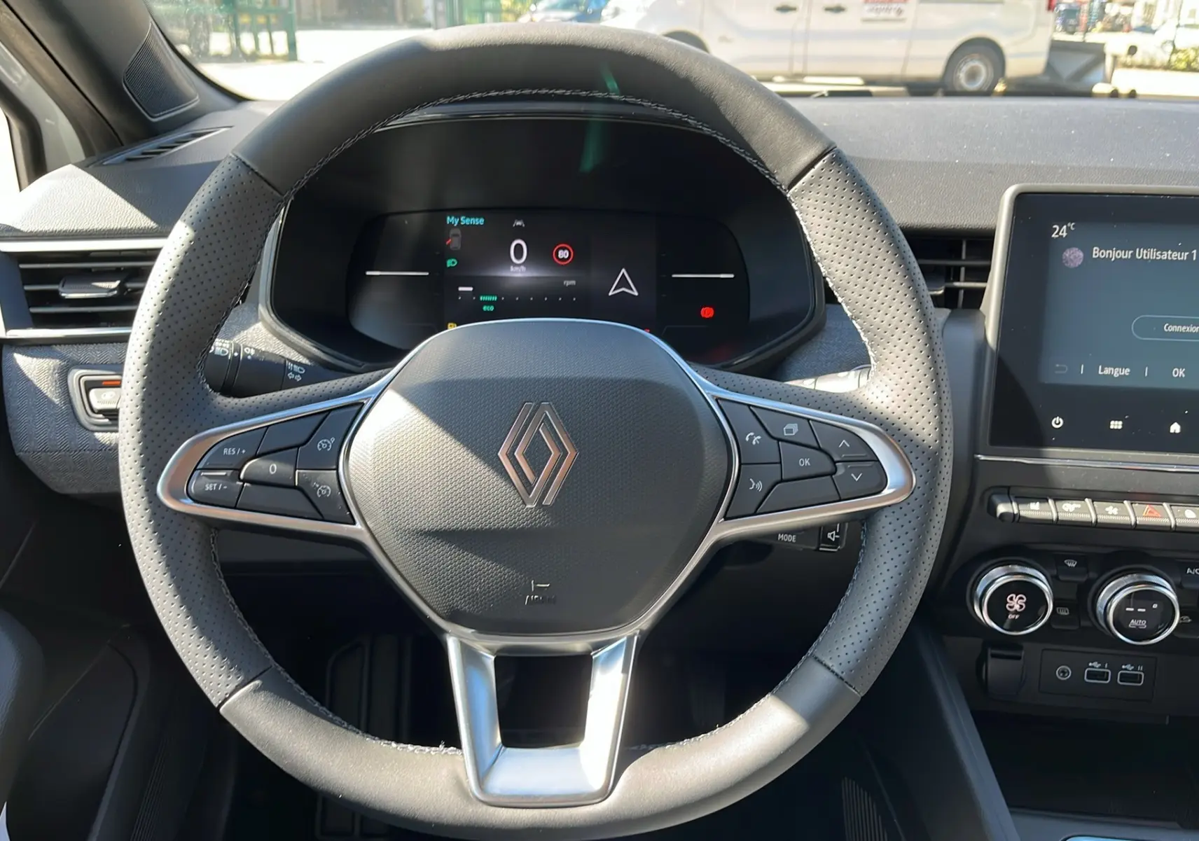 Vue centrée sur le volant perforé de la Renault Clio V Facelift TCe 90 Techno 2025 avec tableau de bord digital et écran tactile.