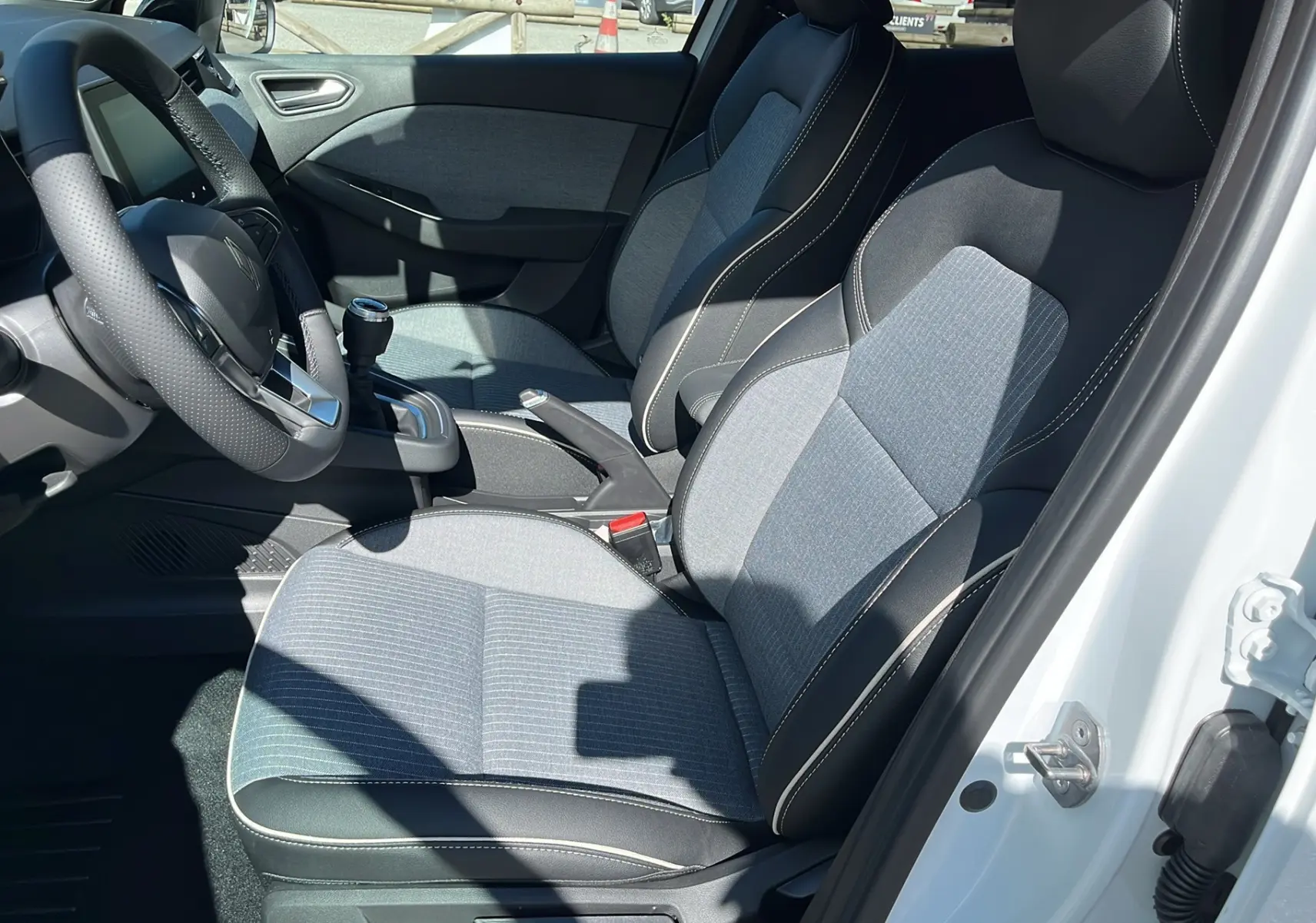 Intérieur de la Renault Clio V Facelift TCe 90 Techno 2025, vue côté conducteur, sièges tissu gris et cuir noir.