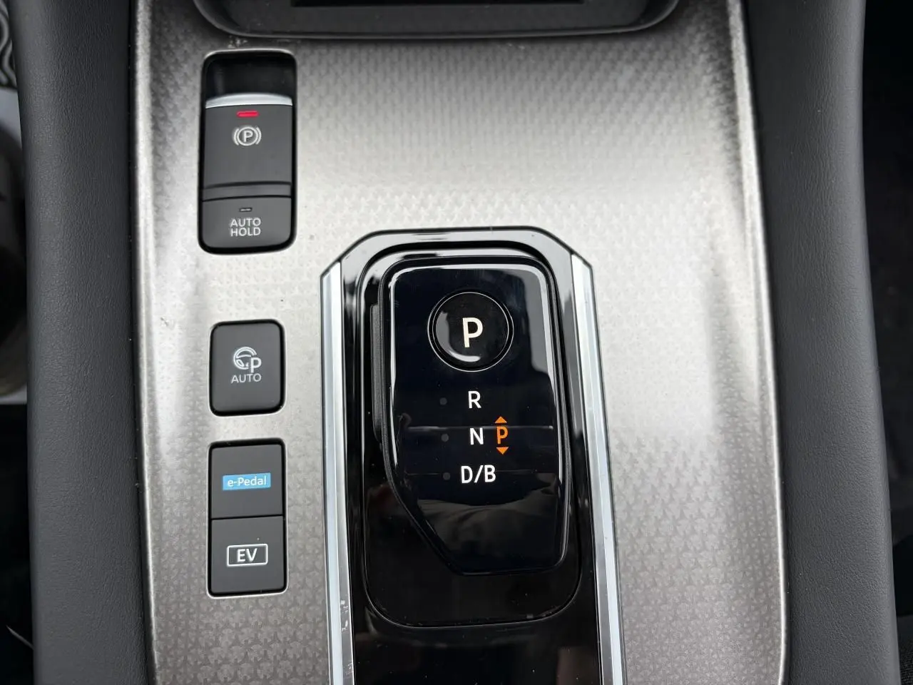 Gros plan sur la console centrale argentée et noire du Nissan Qashqai III 1.5 Hybrid avec sélecteur de boîte auto et boutons de fonctions.