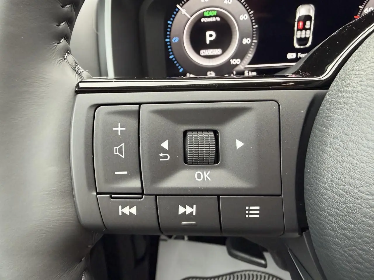 Gros plan sur les commandes au volant noir du Nissan Qashqai 2025, avec écran numérique en arrière-plan.