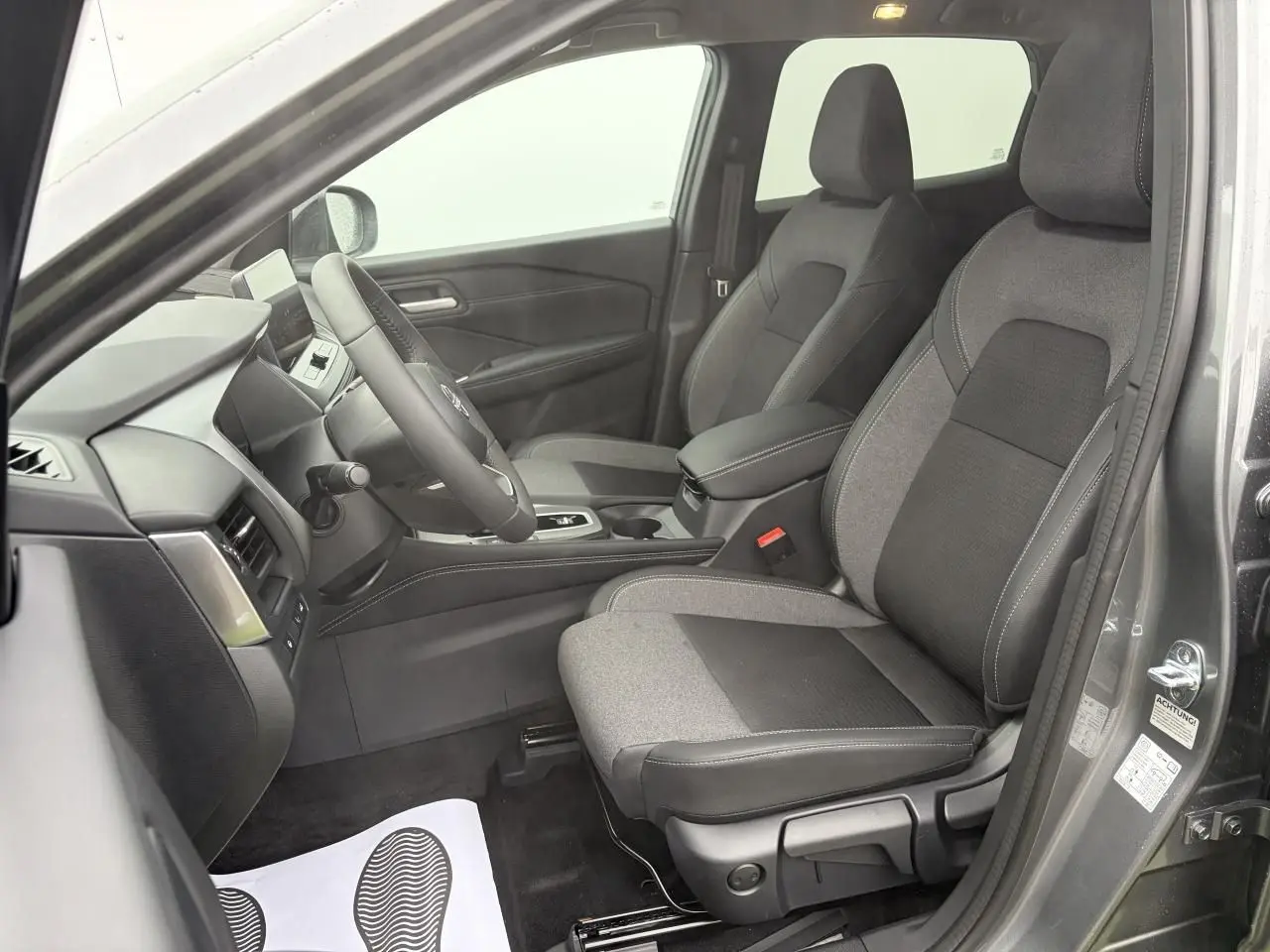 Vue intérieure côté conducteur du Nissan Qashqai III 2025 gris foncé, sièges tissu et TEP noirs avec coutures blanches.