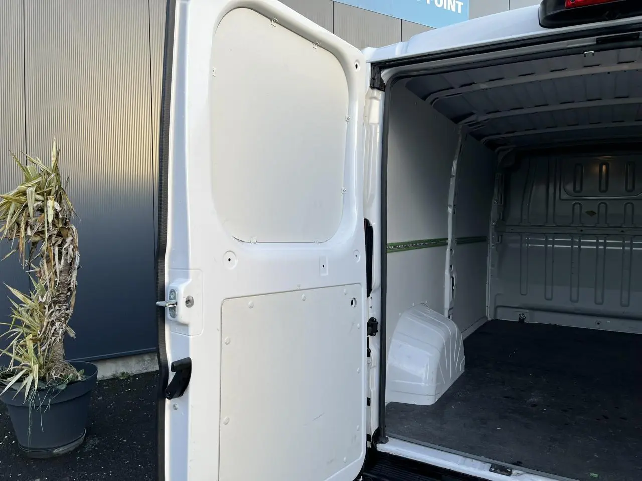 Vue arrière droite du fourgon blanc Opel Movano 2024 avec porte latérale ouverte montrant l'intérieur vide et plancher bois.