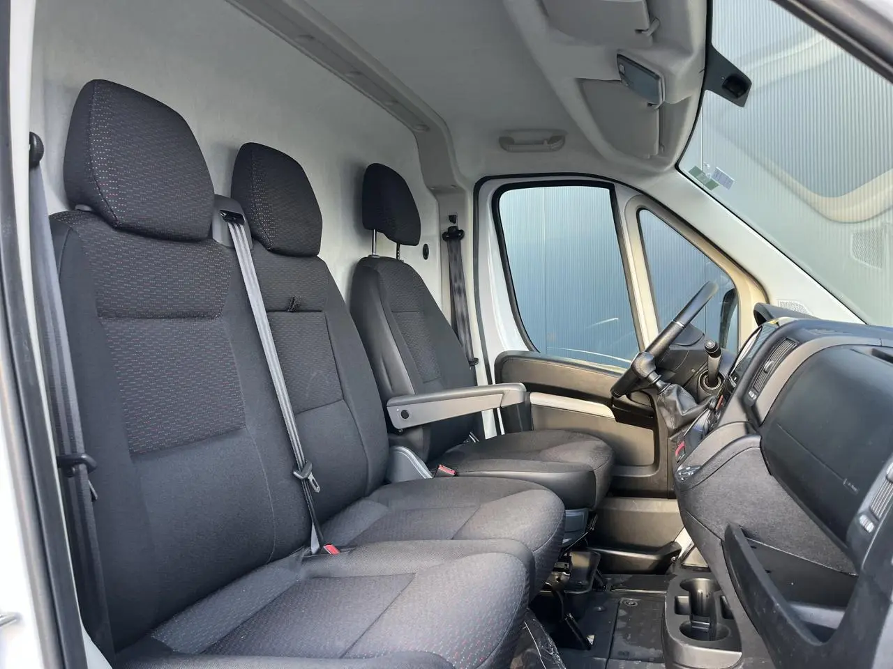 Vue intérieure côté conducteur de l'Opel Movano Fourgon 2024, sièges tissu gris foncé et tableau de bord noir.