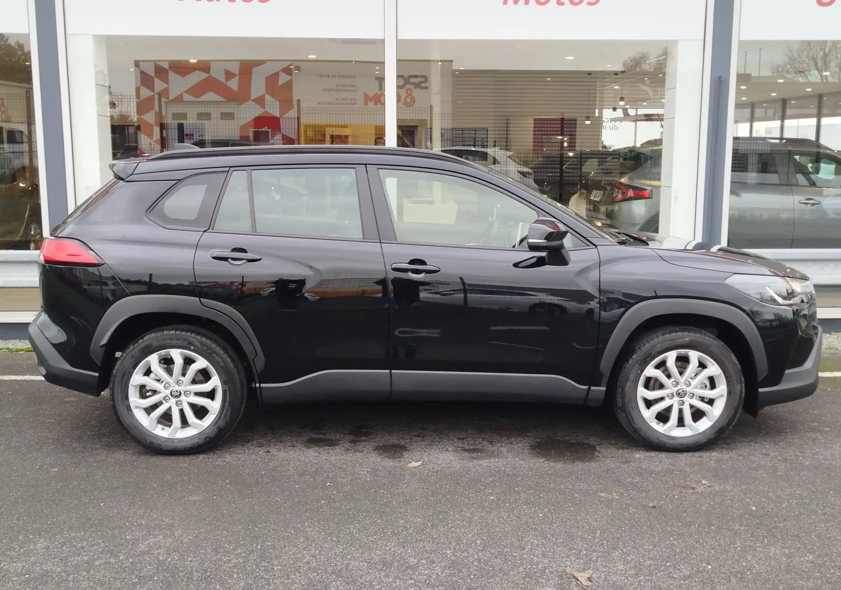 Vue de profil côté gauche d’un Toyota Corolla Cross noir intense 2025, avec jantes alliage et lignes robustes.
