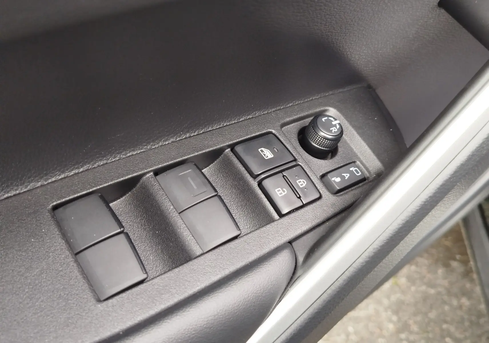 Gros plan sur les commandes de lève-vitres et réglage des rétroviseurs côté conducteur d'une Toyota Corolla Cross noir intense.