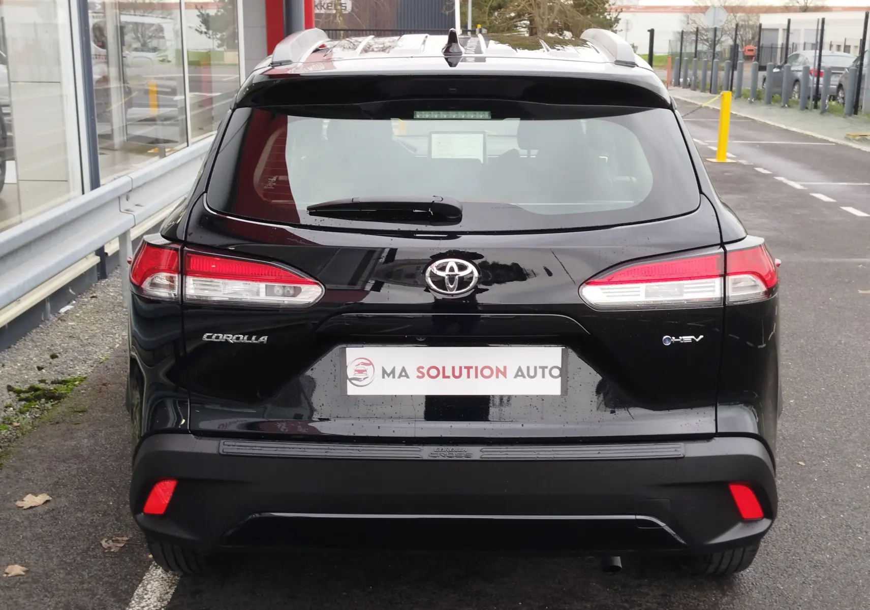 Vue arrière d'une Toyota Corolla Cross noire intense 2025 avec feux LED et logo hybride visible.
