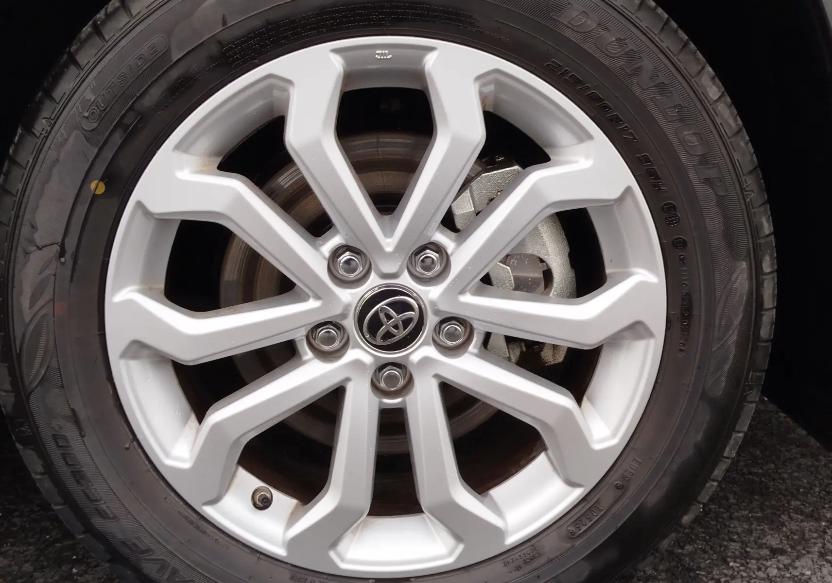 Gros plan sur la jante alliage argentée du Toyota Corolla Cross 2025 noir intense, mettant en valeur le logo Toyota central.