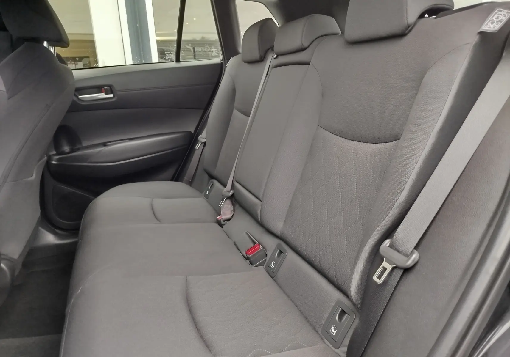 Vue intérieure de la banquette arrière noire intense de la Toyota Corolla Cross 2025, avec ceintures et appuie-têtes visibles.