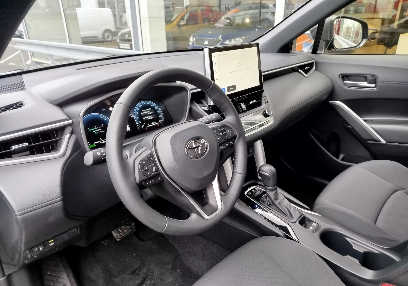 Vue intérieure côté conducteur du Toyota Corolla Cross 2025, tableau de bord moderne avec écran tactile central et volant multifonction noir.