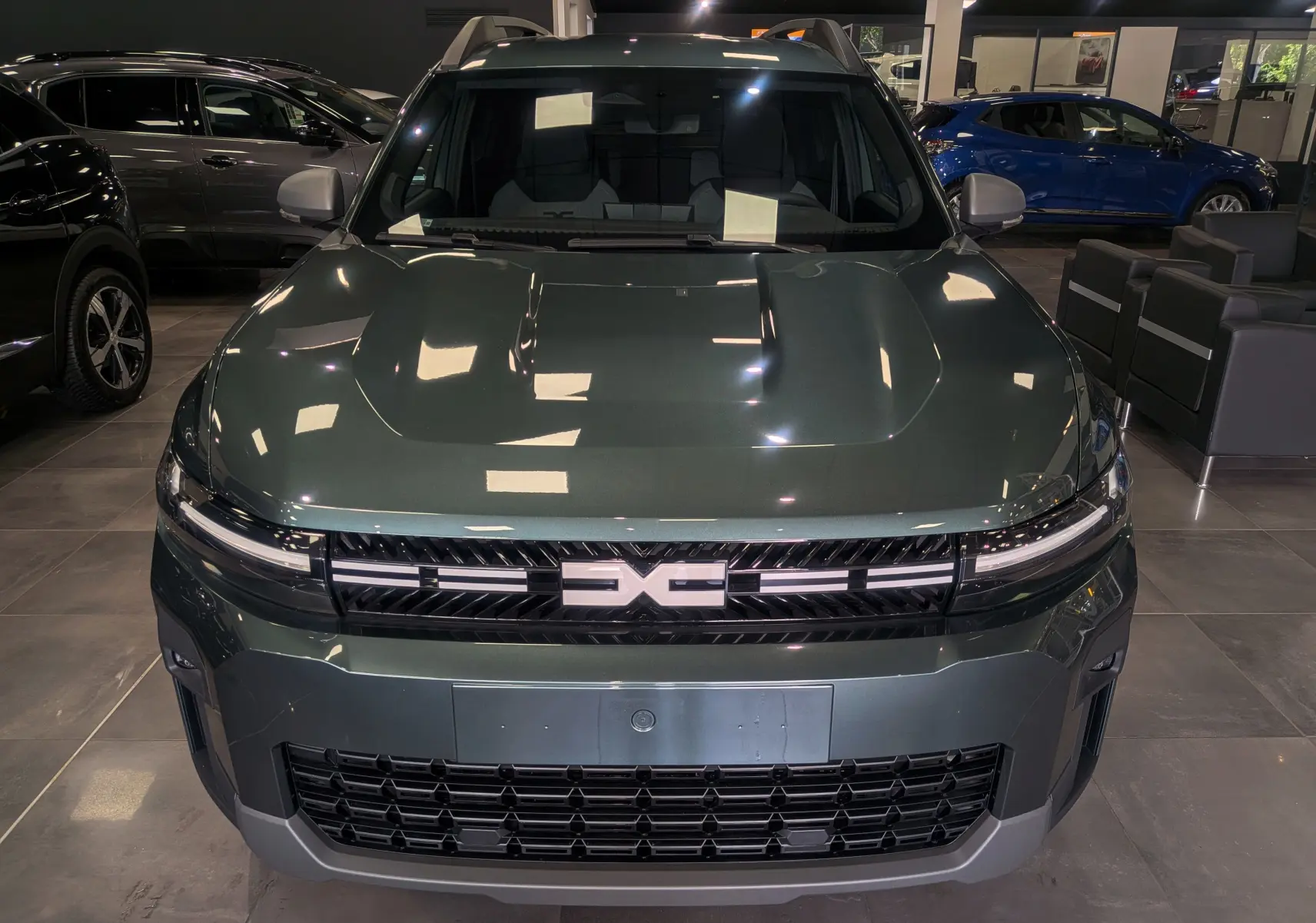 Vue avant d'un Dacia Bigster 2026 vert cèdre en showroom, avec calandre distinctive et phares LED fins.