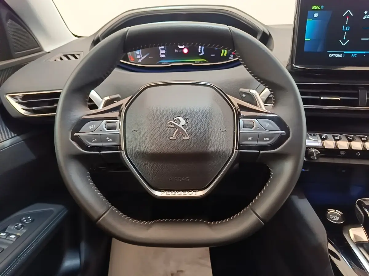Vue rapprochée du volant cuir multifonctions noir du Peugeot 3008 1.6 Hybrid 225, avec tableau de bord digital en arrière-plan.