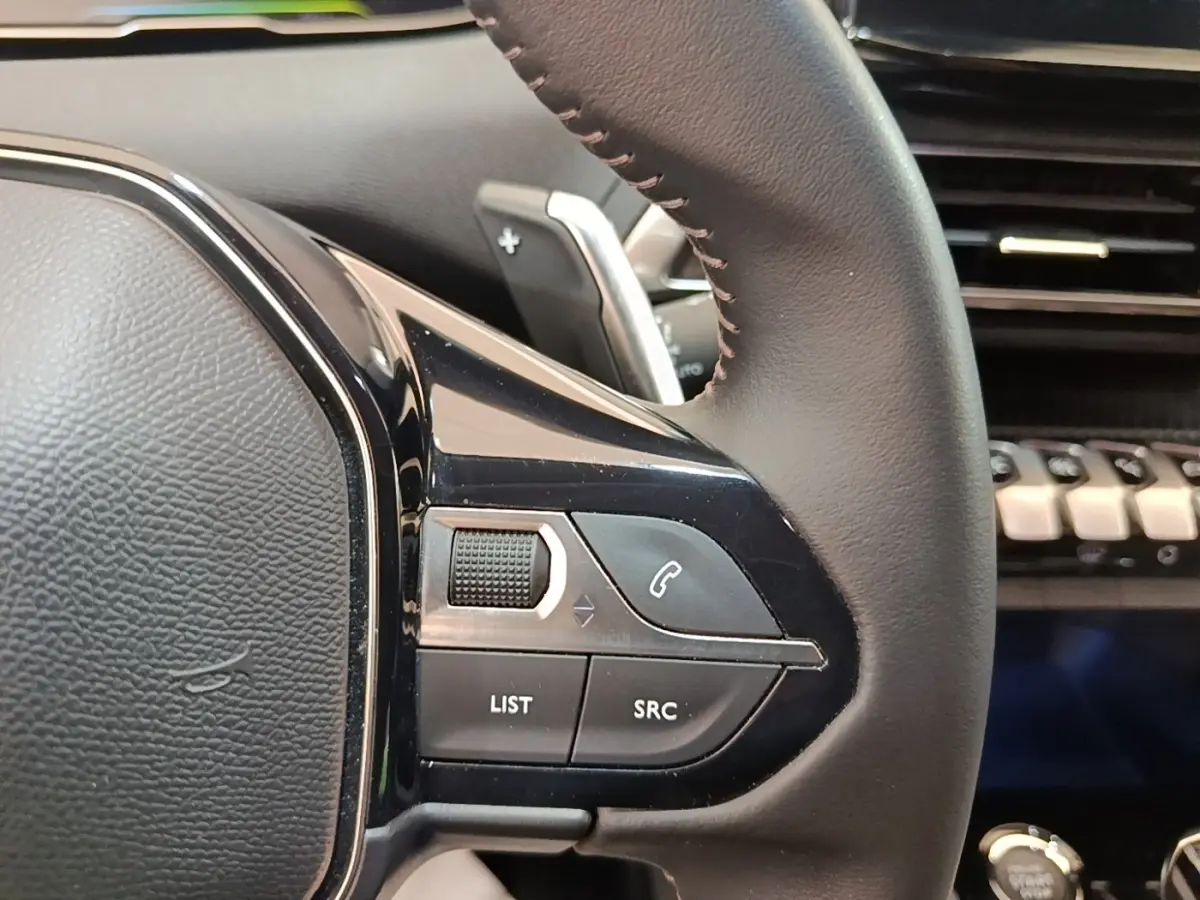 Gros plan sur le côté gauche du volant cuir noir du Peugeot 3008 hybride 2023 avec commandes multifonctions.