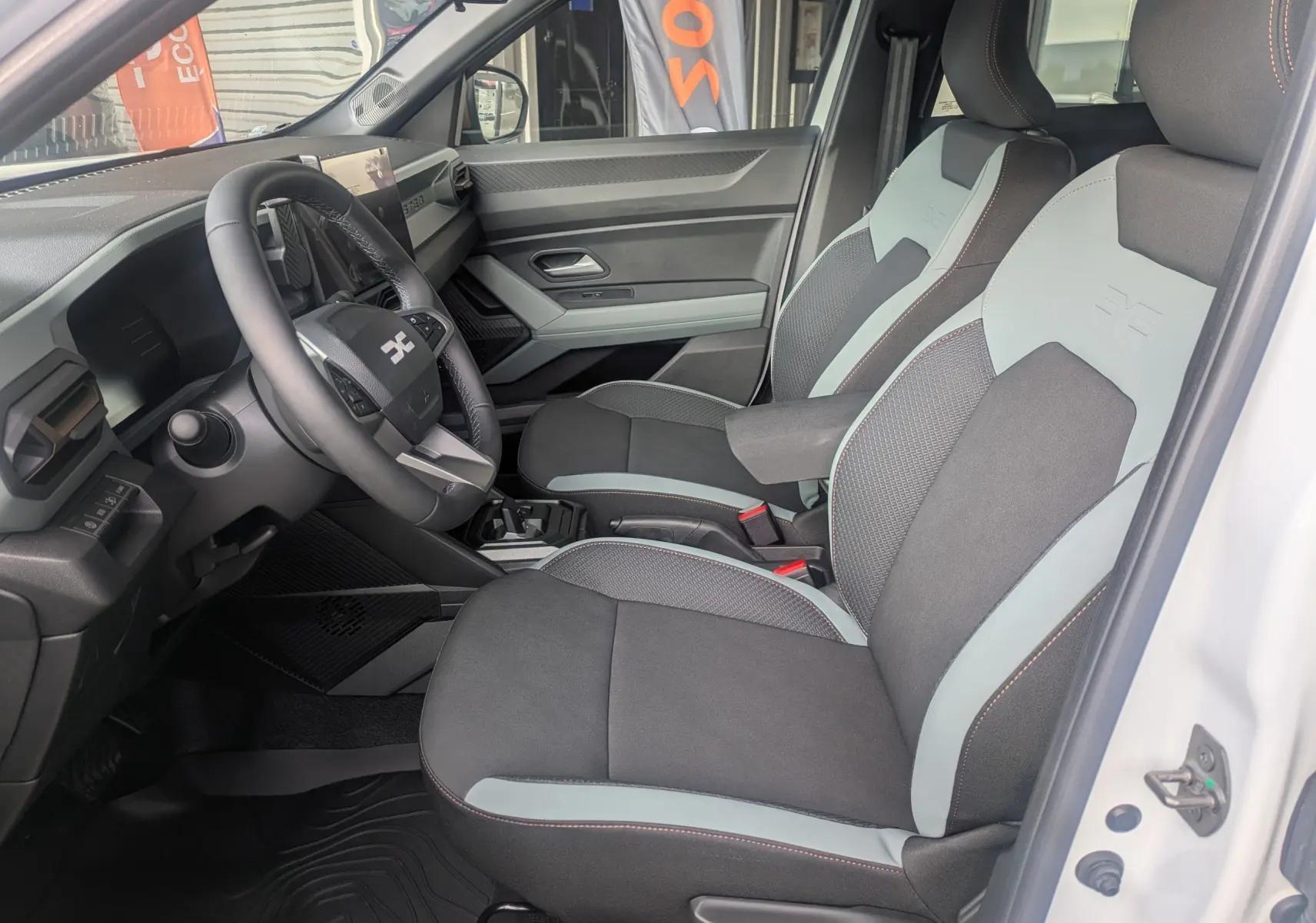 Vue intérieure côté conducteur du Dacia Duster Hybrid 155 Extreme blanc glacier, sièges tissu bicolore avec logo embossé.