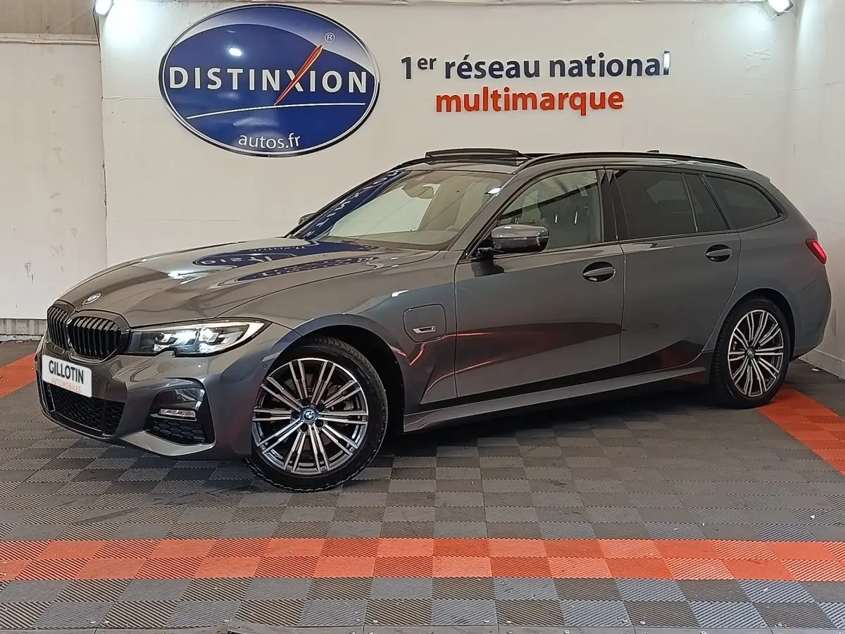 BMW Série 3 320e M Sport gris foncé en break, vue de profil côté droit avec jantes alliage et phares allumés.