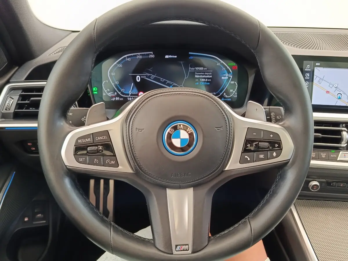 Vue rapprochée du volant cuir noir BMW M Sport avec tableau de bord digital et écran tactile de navigation.