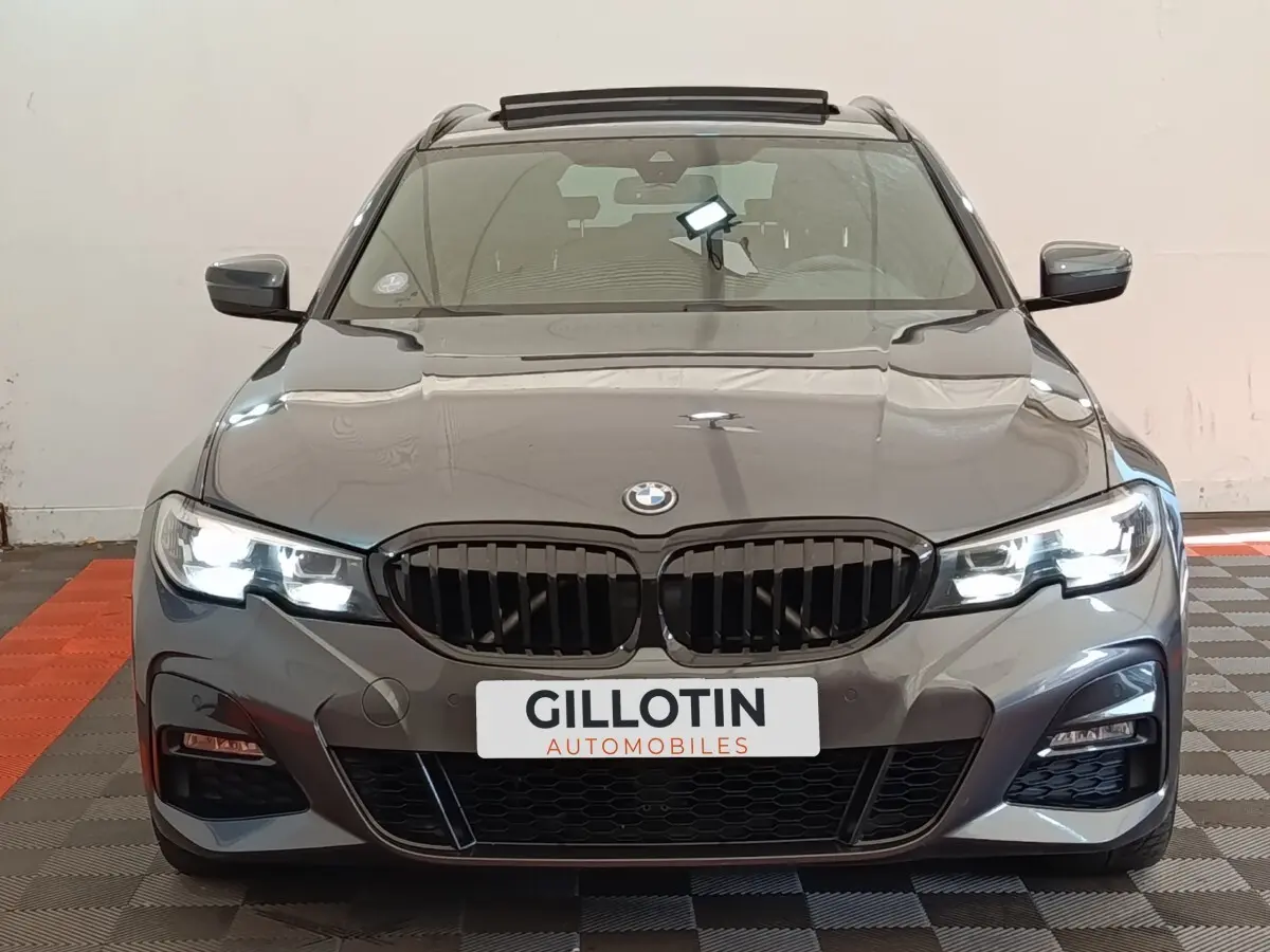 Vue frontale d'une BMW Série 3 320e M Sport gris foncé avec phares LED allumés en intérieur.