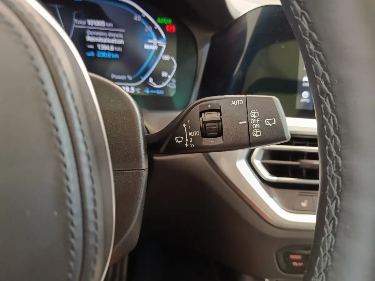 Gros plan sur la commande d’essuie-glace à gauche du volant dans l’habitacle d’une BMW Série 3 gris foncé 320e hybride.