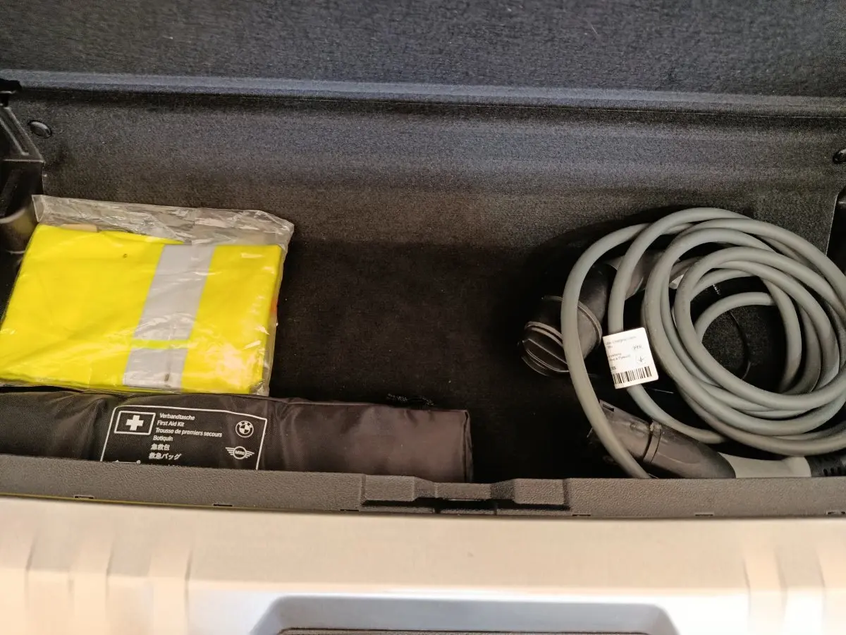 Coffre ouvert d’une BMW Série 3 320e gris foncé, montrant câble de charge et trousse de premiers secours.