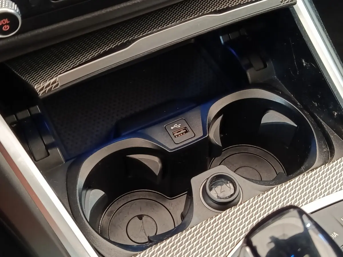 Gros plan sur les porte-gobelets et prise USB du coffre central d’une BMW Série 3 320e gris foncé hybride rechargeable.