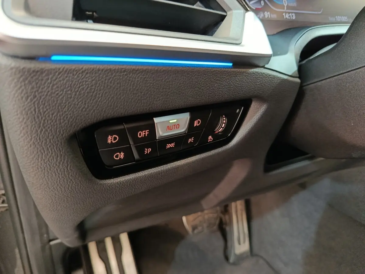 Détail du panneau de commandes d’éclairage avec bouton auto, sur le côté gauche du tableau de bord d’une BMW Série 3 gris foncé.