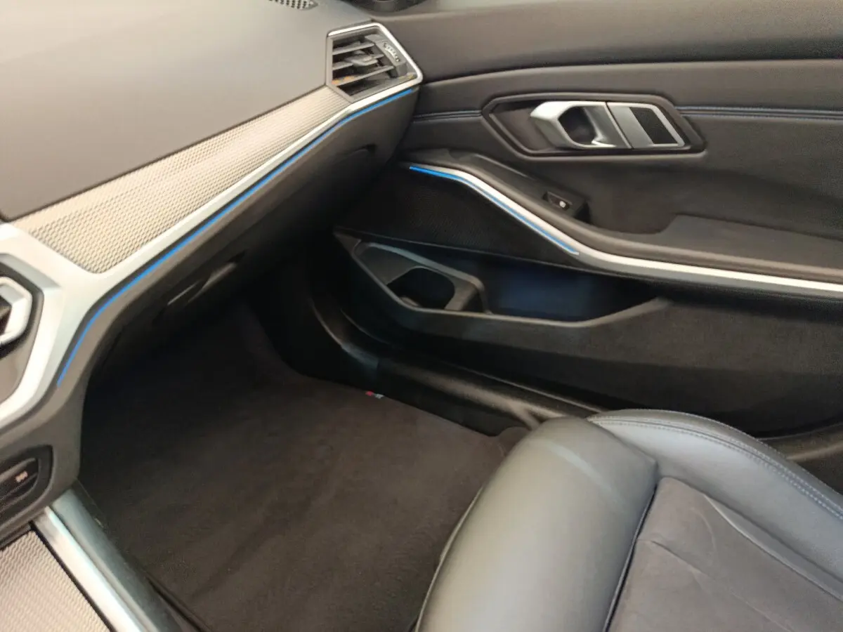 Vue intérieure côté passager avant de la BMW Série 3 320e gris foncé, avec détails du tableau de bord et porte en cuir noir.