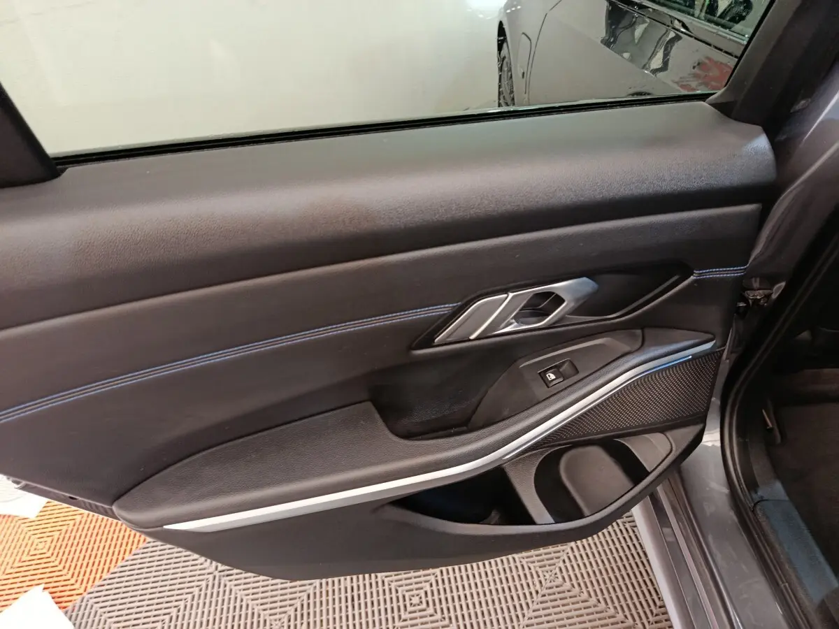 Vue intérieure de la porte arrière droite d'une BMW Série 3 320e gris foncé avec garniture noire et surpiqûres bleues.