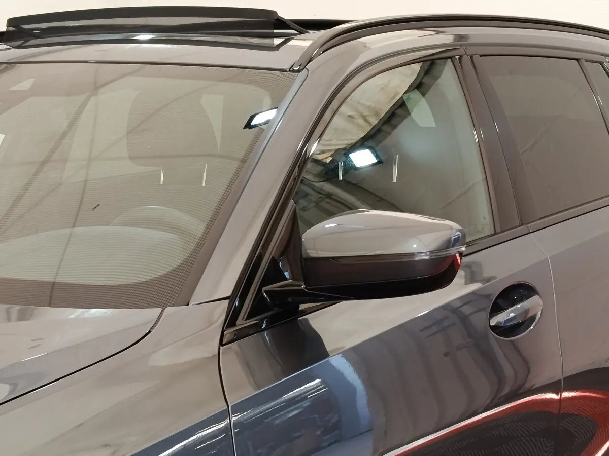 Vue rapprochée côté gauche d’une BMW Série 3 320e M Sport gris foncé avec rétroviseur et poignée de porte visibles.