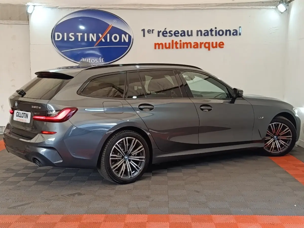 BMW Série 3 320e M Sport gris foncé vue de profil droit en break avec jantes alliage et feux arrière LED allumés.