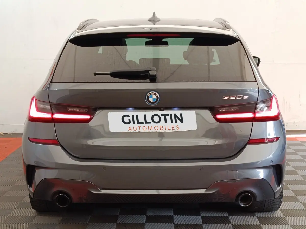 Vue arrière d'une BMW Série 3 320e hybride gris foncé avec feux LED allumés en intérieur.
