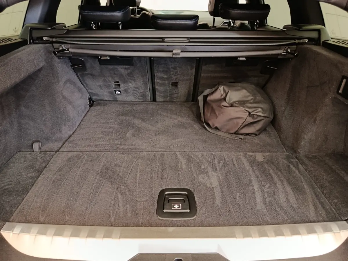 Coffre spacieux de BMW Série 3 320e gris foncé vu de l'arrière avec cache-bagages et sac noir posé.