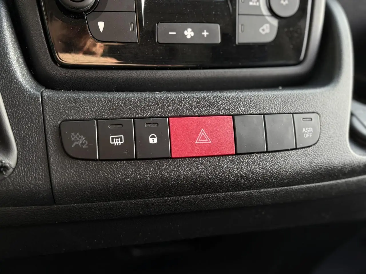 Gros plan sur les boutons de commande noirs et rouge du tableau de bord de l’Opel Movano Fourgon blanc, version 2024.