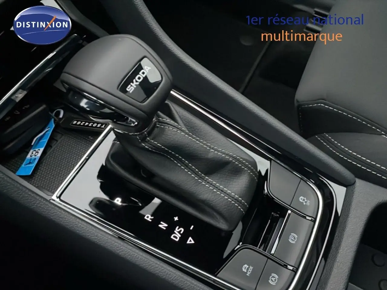 Gros plan sur le levier de vitesses automatique noir avec logo SKODA, entouré de commandes sur console brillante intérieure.