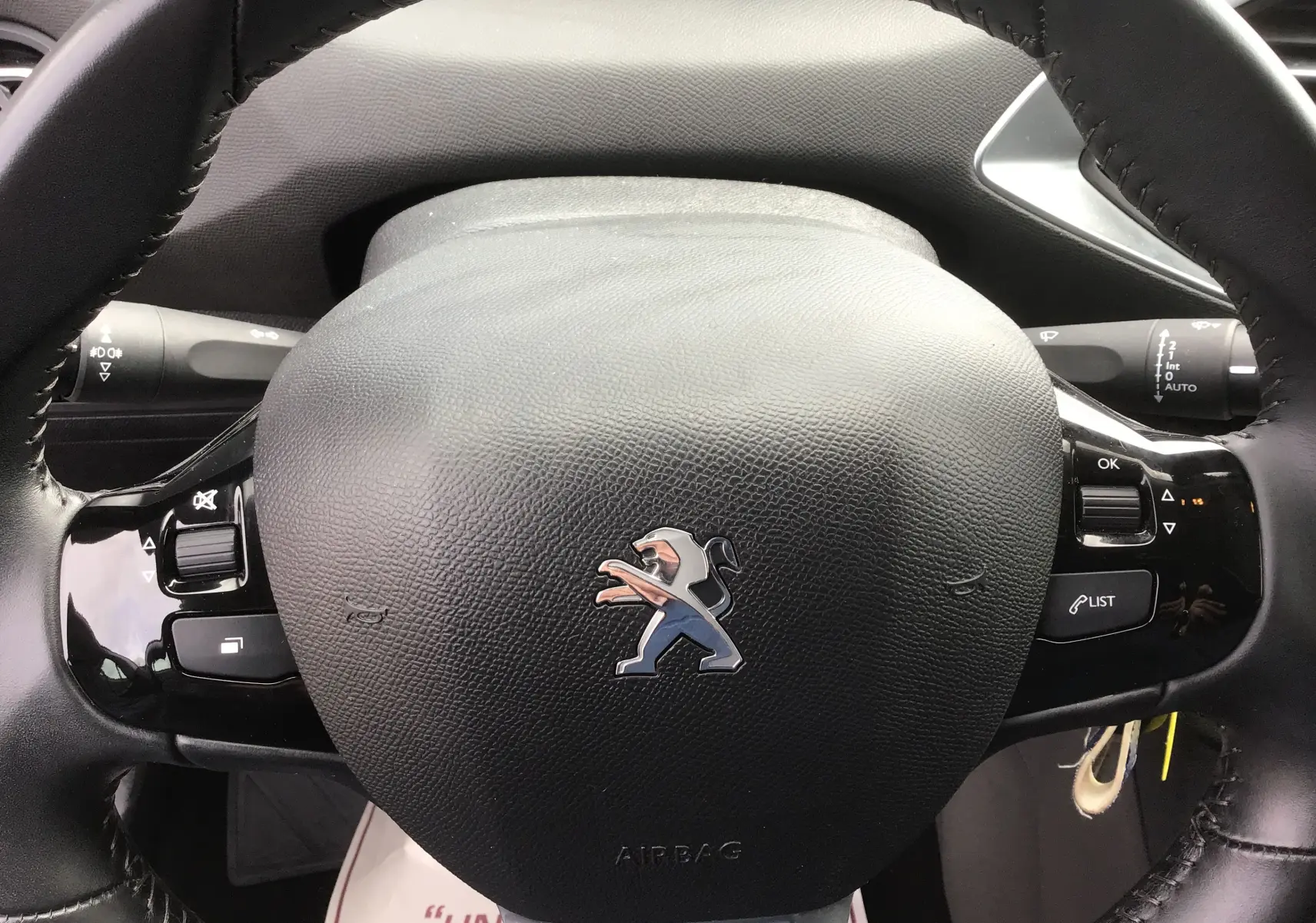 Gros plan sur le volant en cuir noir du Peugeot 308 gris Artense, avec commandes intégrées et logo lion central.