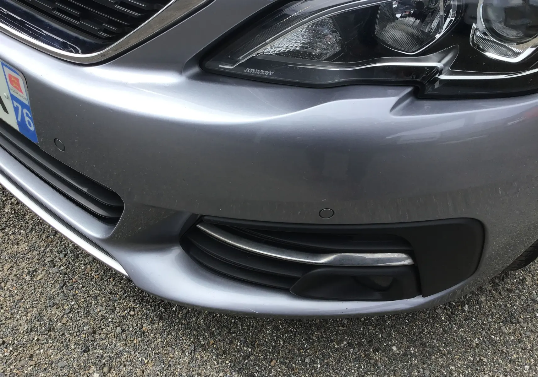 Gros plan sur l’avant droit gris Artense de la Peugeot 308 1.5 BlueHDi 100, avec phare et calandre visibles.