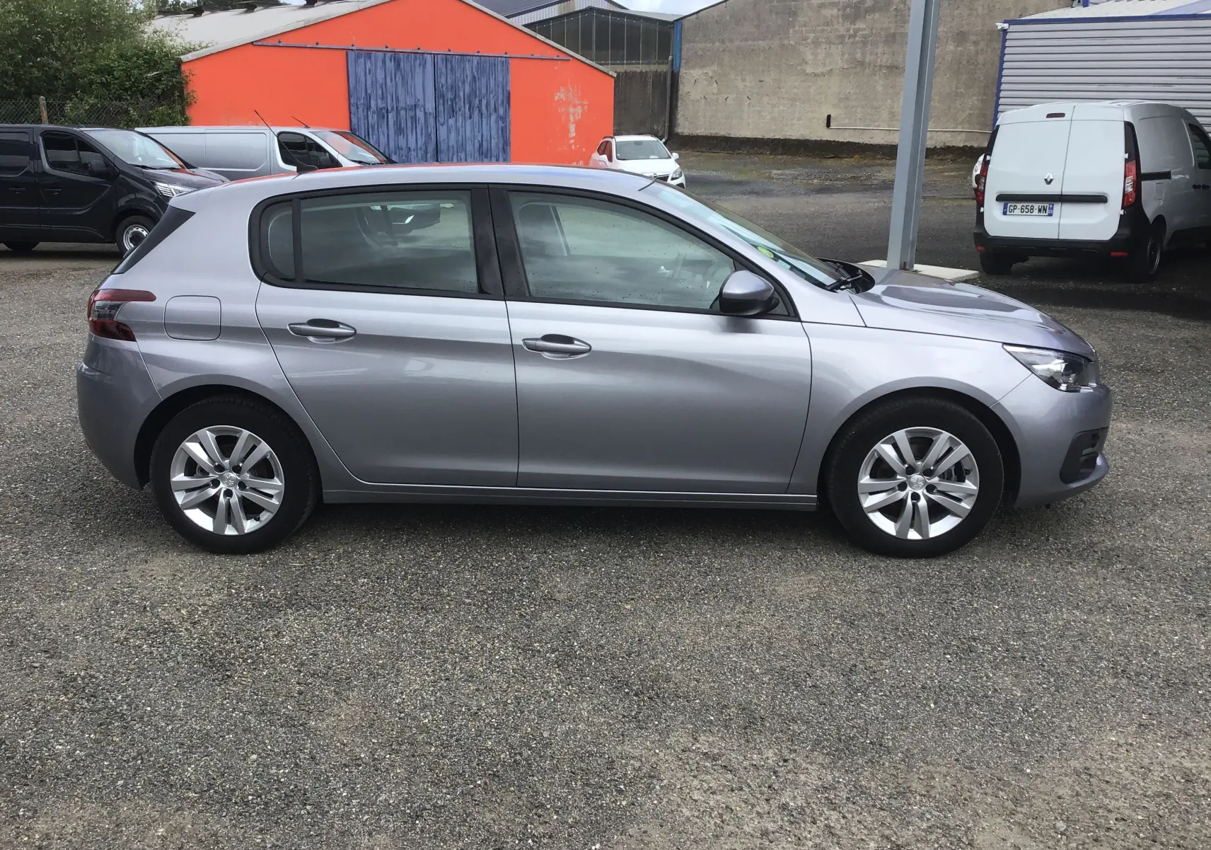 Peugeot 308 gris Artense vue de profil côté gauche, compacte et moderne sur un parking extérieur.