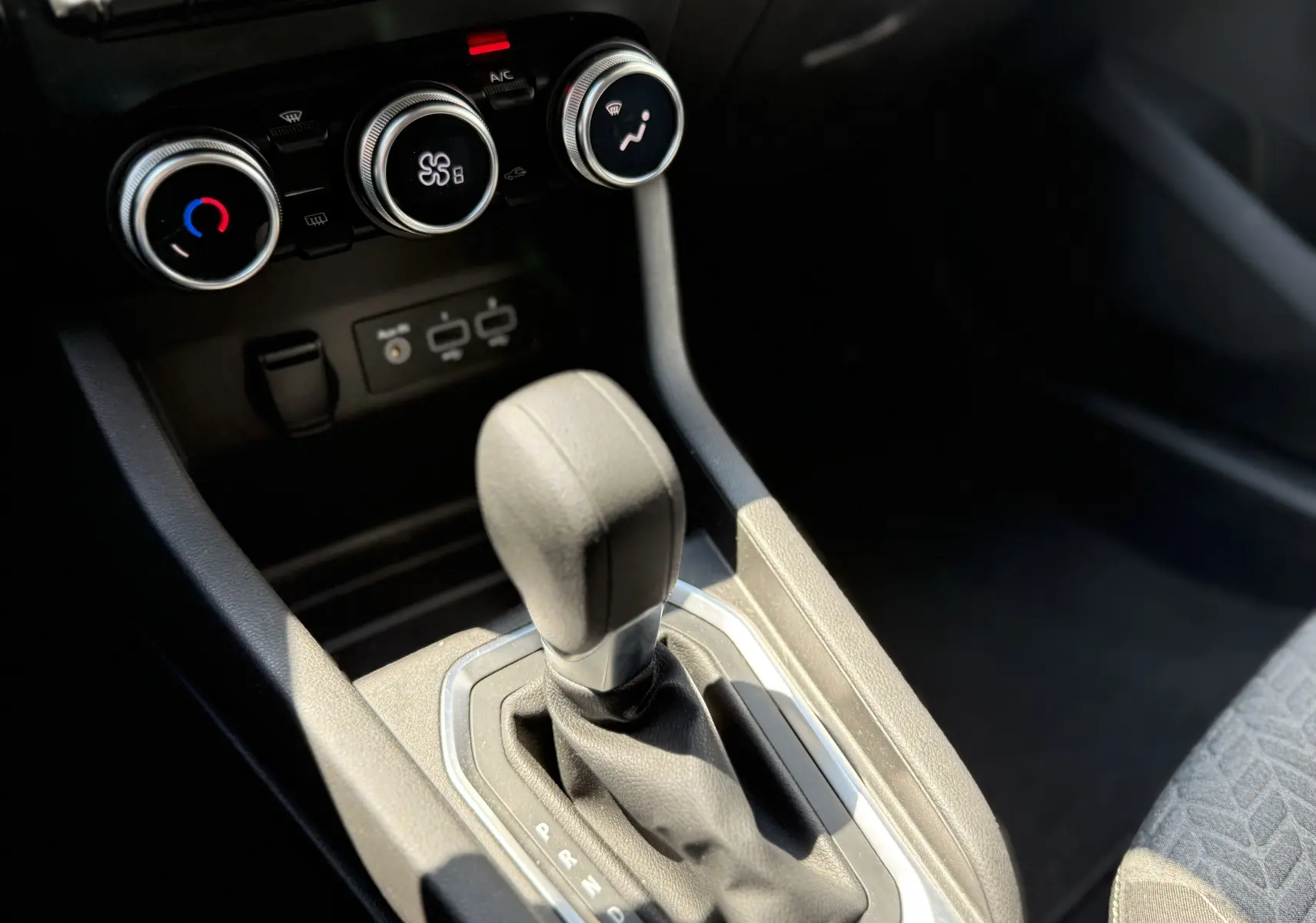 Gros plan sur le levier de vitesse automatique et les commandes de climatisation d’une Renault Clio V gris, intérieur noir.