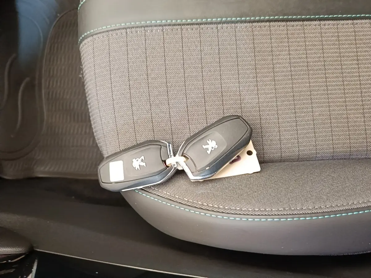 Clé de démarrage Peugeot posée sur le siège avant gris foncé avec surpiqûres bleues, intérieur du véhicule visible.