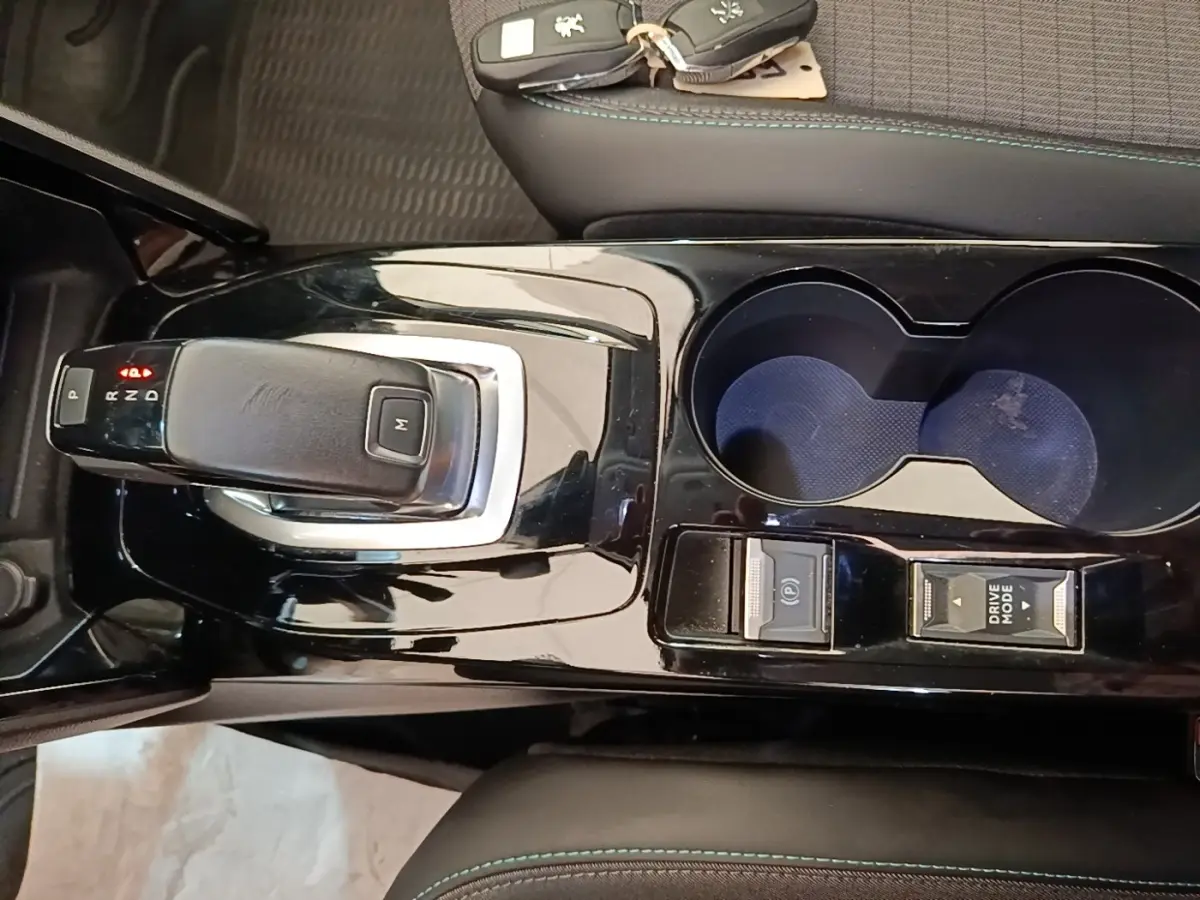 Vue plongeante sur la console centrale noire brillante du Peugeot 2008 gris clair avec levier de boîte auto et porte-gobelets.