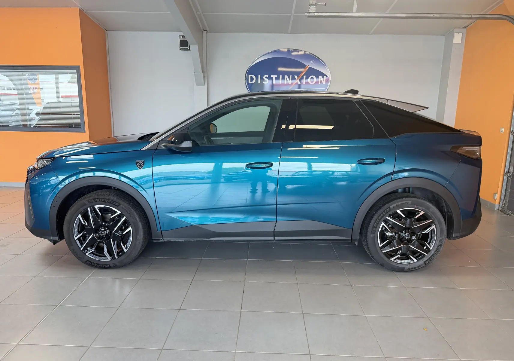 Vue de profil côté gauche du Peugeot 3008 Hybrid 145 GT bleu obsession avec toit noir et jantes alliage 19 pouces en intérieur showroom.