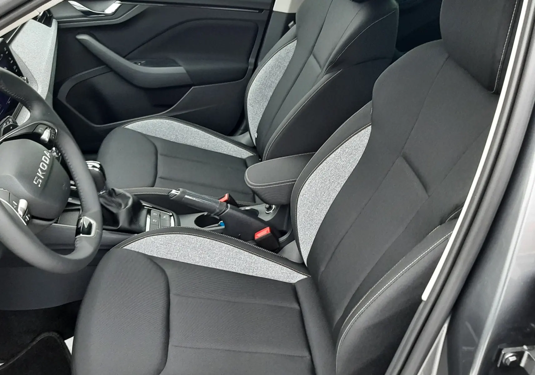 Intérieur du Skoda Kamiq 2025 en gris graphite métal, vue côté gauche sur sièges tissu noir et gris avec coutures contrastées.