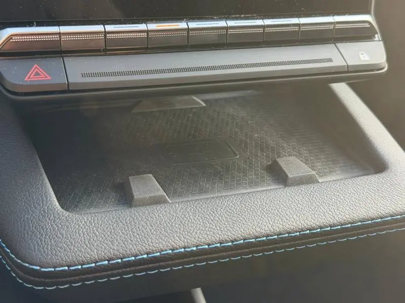 Gros plan sur la console centrale noire avec surpiqûres bleues du Renault Scenic E-Tech Electric 2025, zone de recharge sans fil visible.
