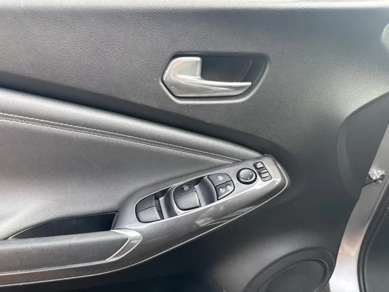 Détail de la porte avant gauche gris perle métallisé du Nissan Juke 2022 avec commandes électriques et poignée chromée.