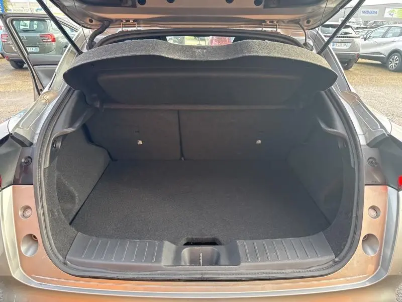 Coffre ouvert vu de l'arrière d'un Nissan Juke gris perle métallisé, montrant un espace de chargement propre et vide.