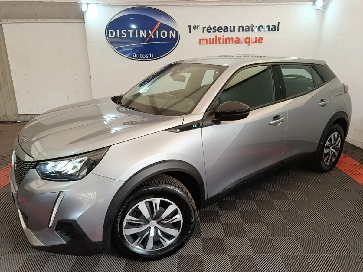 Peugeot E-2008 électrique gris clair en 3/4 avant droit, avec jantes spécifiques et rétroviseurs noirs brillants.