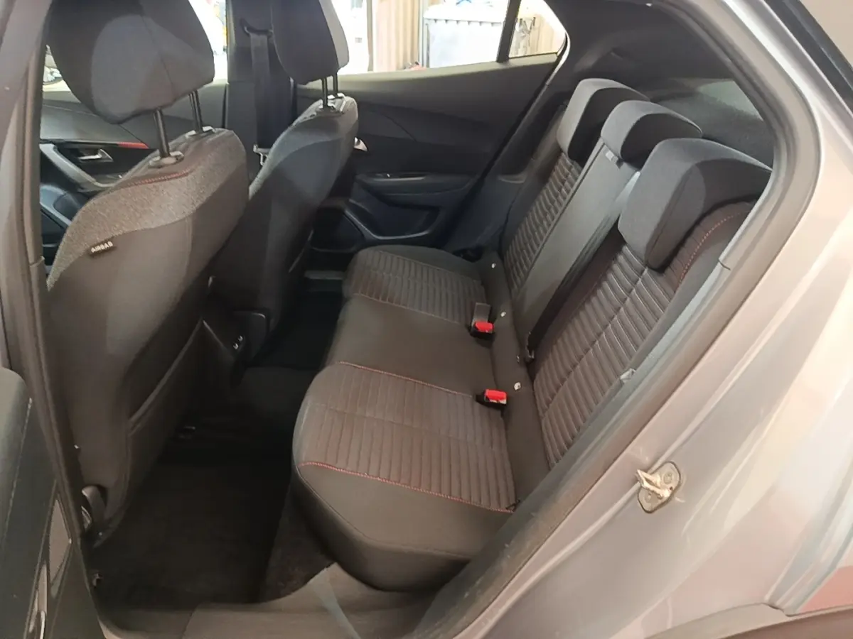 Vue intérieure côté droit sur la banquette arrière noire avec surpiqûres rouges du Peugeot E-2008 électrique gris clair.