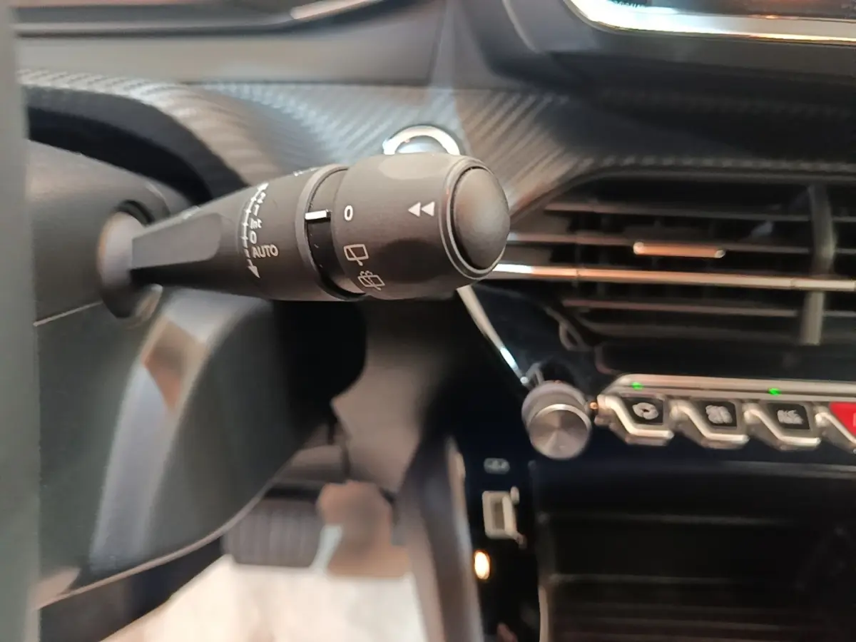 Gros plan sur la commande d'essuie-glace à gauche du volant dans l'habitacle noir du Peugeot E-2008 électrique gris clair.