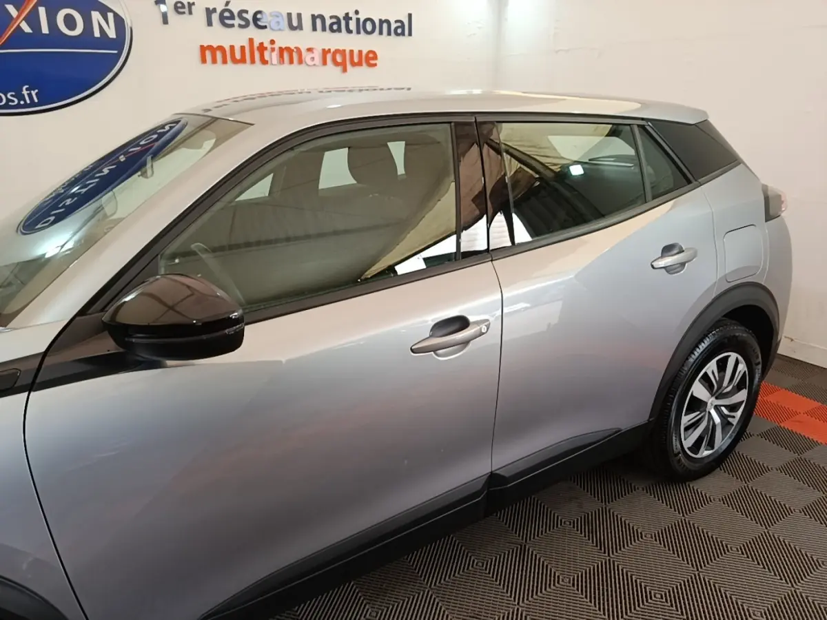 Vue de profil côté gauche du Peugeot E-2008 électrique gris clair, avec rétroviseur noir et jantes distinctives.