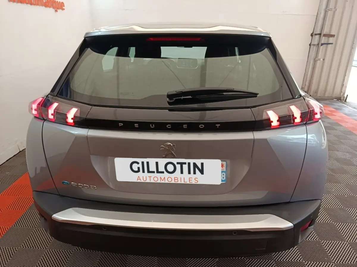Vue arrière d'un Peugeot E-2008 électrique gris clair avec feux LED caractéristiques et logo central sur hayon.